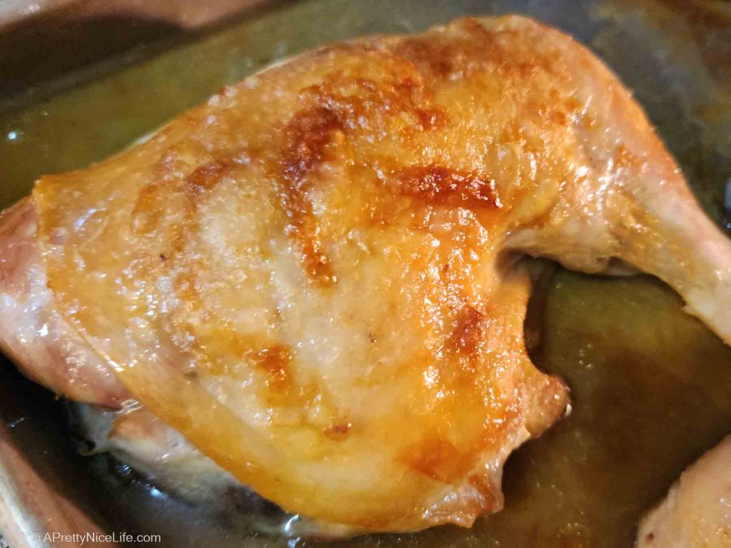 Close-up of juicy, golden-brown roasted chicken leg quarter still on the pan, fresh from the oven.