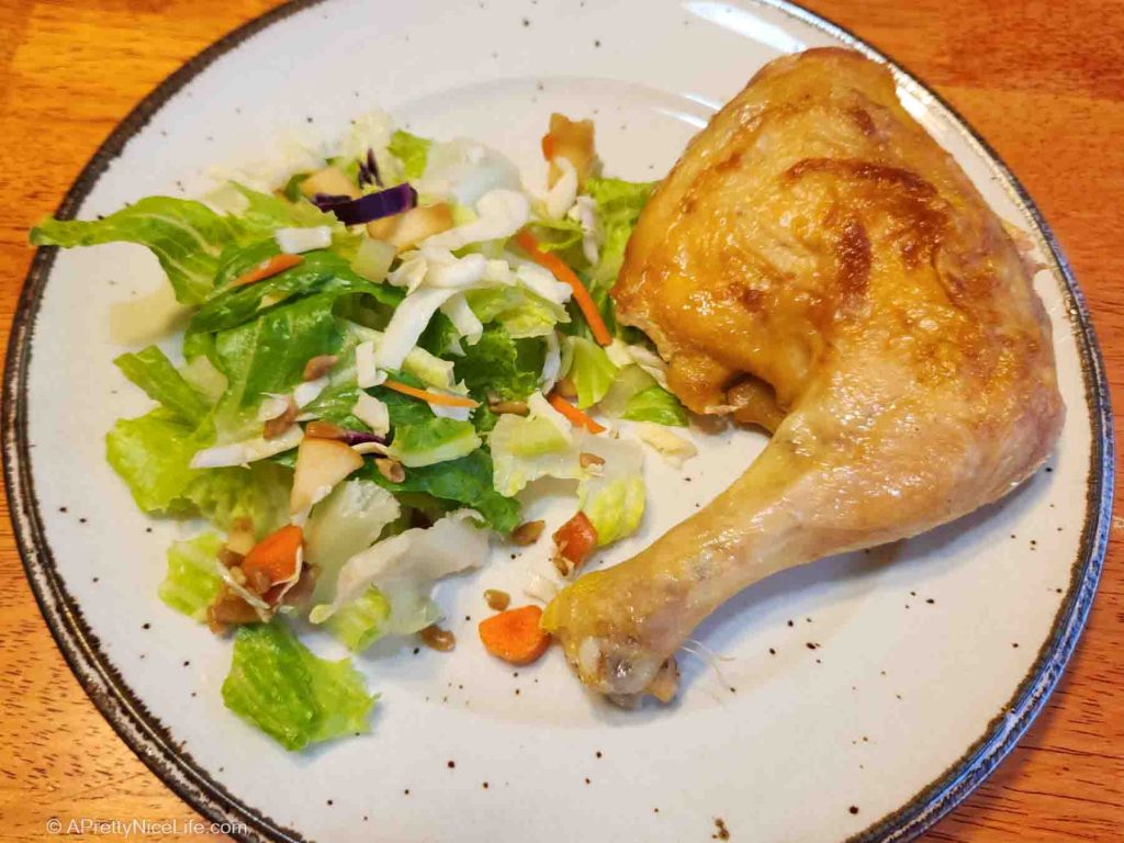 Plate with juicy oven-roasted chicken leg quarter next to green salad.
