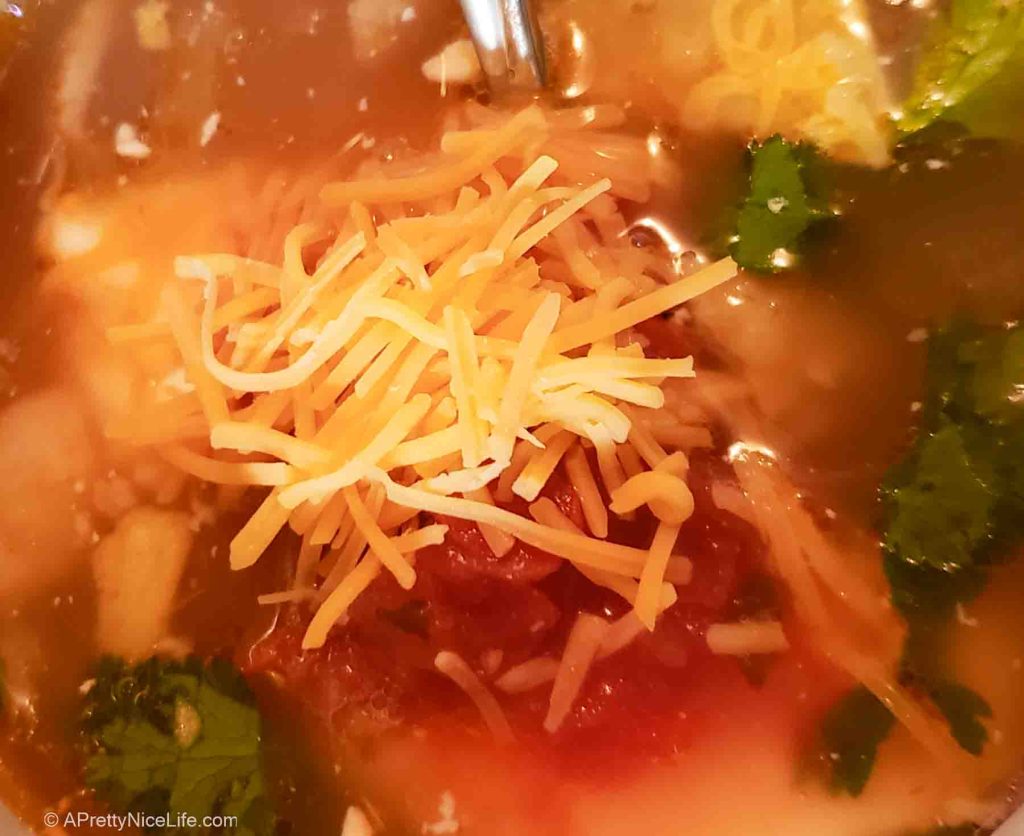 close-up of chicken tortilla soup topped with shredded cheese and fresh cilantro with tomatoes in a silky broth