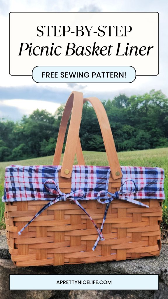 Cute custom fabric picnic basket liner peeking over the top of a picnic basket set on a stone ledge, with a green meadow and trees in the background.