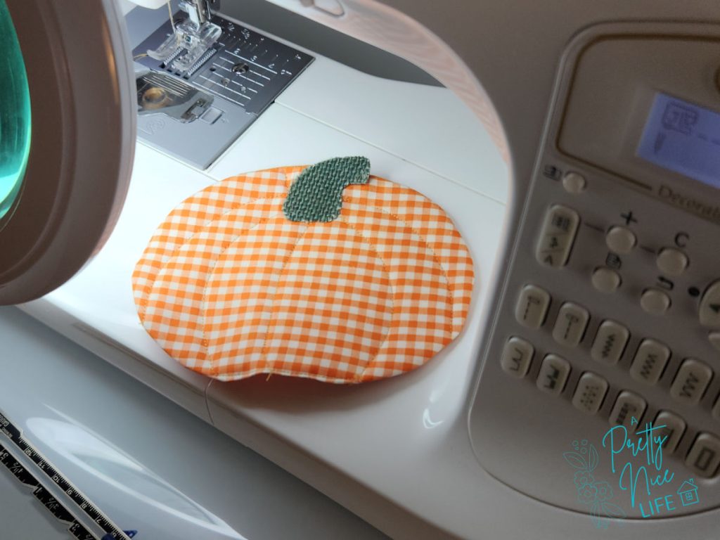 Orange gingham quilted pumpkin coaster turned right side out on a sewing machine, ready for rib line quilting