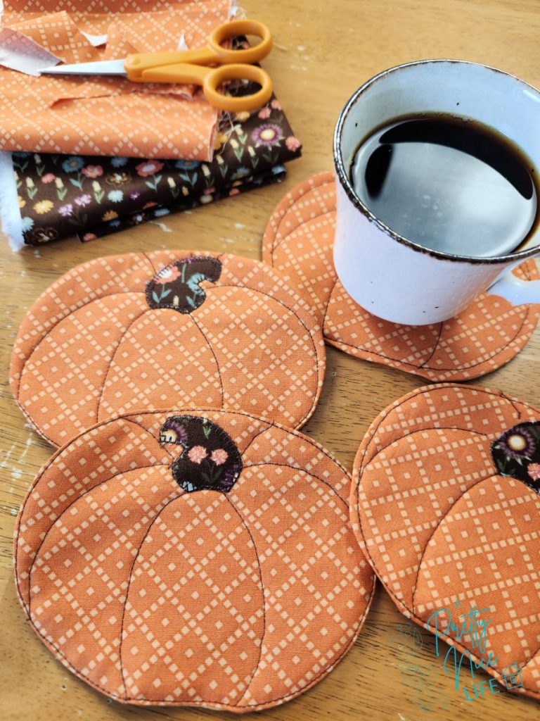Set of quilted fall fabric pumpkin coasters in orange print fabric arranged on a wood table with a coffee cup