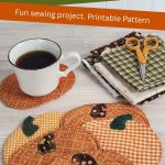 Six quilted fabric pumpkin coasters on a wood table with a coffee cup resting on one. Fall fabric scraps and small scissors are visible in the background. Text reads: "Fall Pumpkin Fabric Coasters. Fun Sewing Project. Printable Pattern. Aprettynicelife.com"