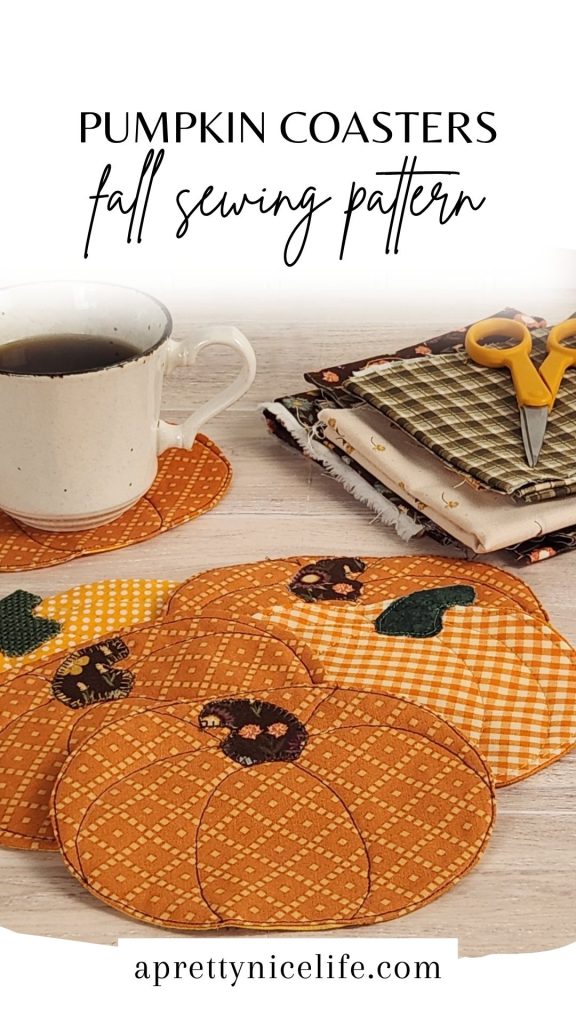 Six quilted fabric pumpkin coasters on a wood table with a coffee cup resting on one. Fall fabric scraps and small scissors are visible in the background. Text reads: "Pumpkin Coasters. Fall Sewing Pattern. Aprettynicelife.com"