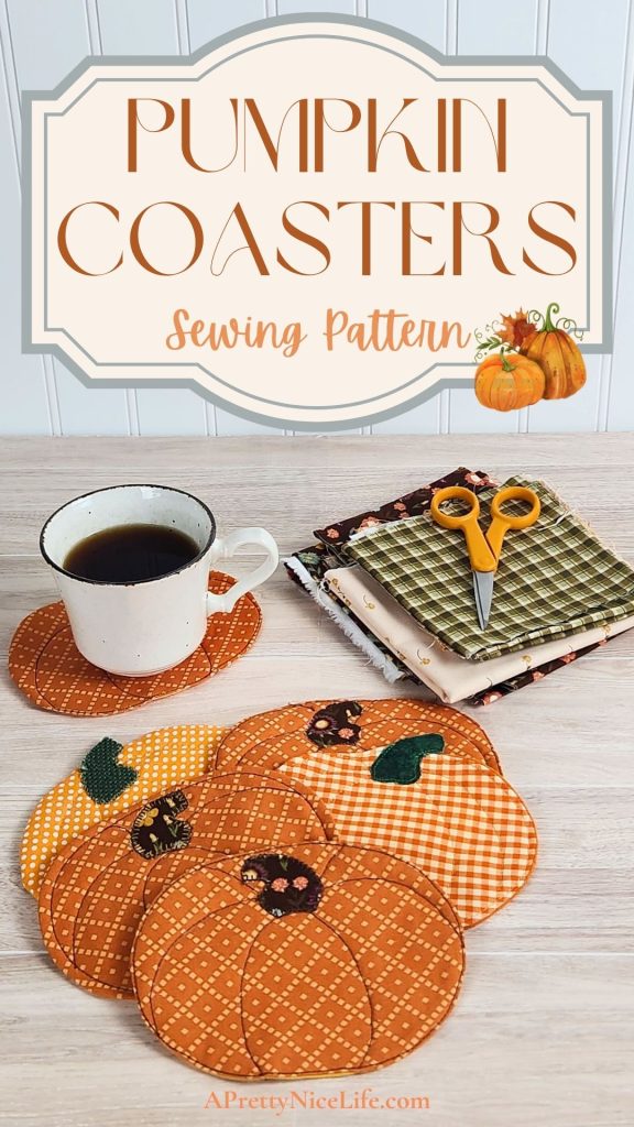Six quilted fabric pumpkin coasters on a wood table with a coffee cup resting on one. Fall fabric scraps and small scissors are visible in the background. A decorative banner with harvest pumpkin graphics frames the text: "Pumpkin Coasters Sewing Pattern APrettyNiceLife.com"