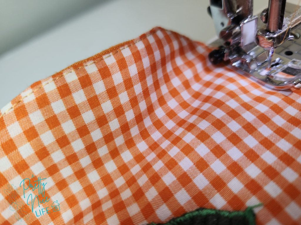 Topstitching around the edge of a gingham fabric pumpkin coaster at the sewing machine to close and finish