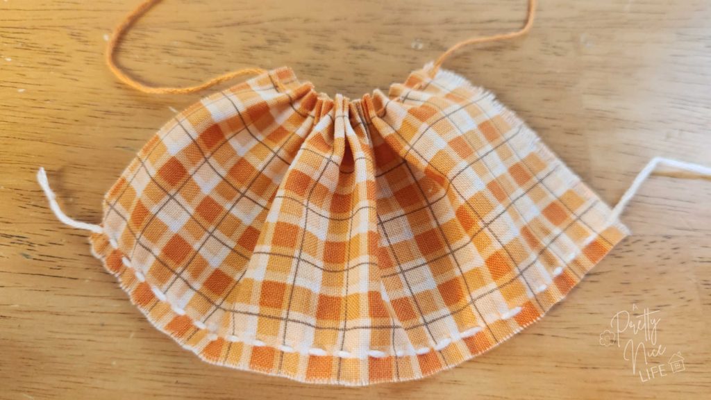Orange and cream colored plaid fabric with one edge gathered.