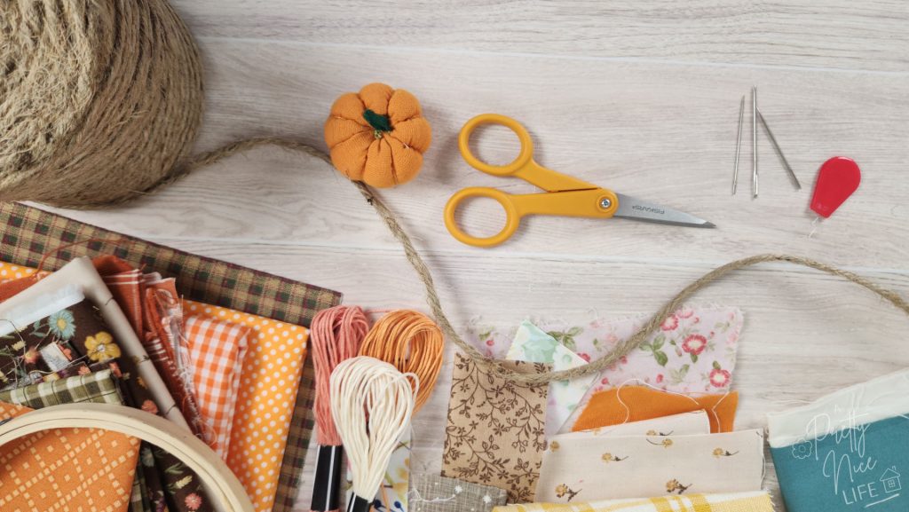 Scattered fabric scraps, embroidery floss, sewing needles, small scissors and twine - ingredients needed for this fun fall pumpkin sewing craft. 