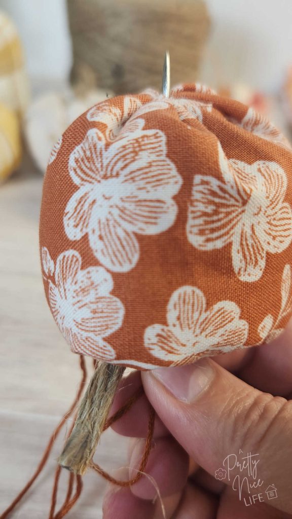 The point of the needle shown pushing out through the bottom of the fabric pumpkin DIY project. 