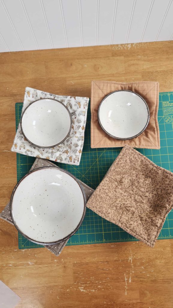 Three bowls in bowl cozies, and one empty handmade bowl cozy, all sitting on a green self-healing cutting mat for sewing projects